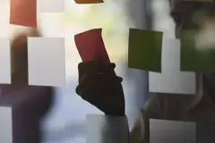 Hand klebt Post-It auf eine Glasscheibe.