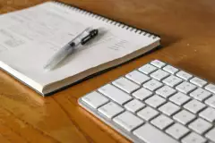 Holztisch mit Tastatur, weißem Stift und Kalender
